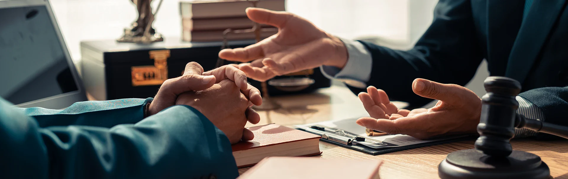 A legal consultation scene showing two professionals discussing over a desk with books, a gavel, and a laptop, emphasizing engagement.
